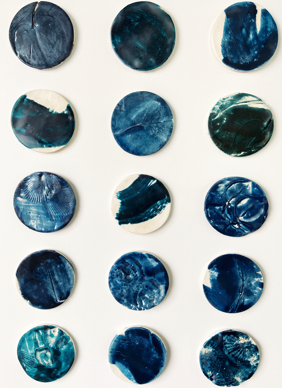 Custom dimensional wall art |composed of 15, 4" diameter clay circular elements with plant and shell impressions, wax encaustic finish mounted on 32.25"H x 20.25"W painted backer