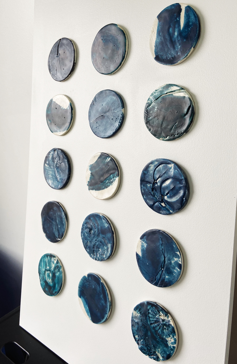 Custom dimensional wall art |composed of 15, 4" diameter clay circular elements with plant and shell impressions, wax encaustic finish mounted on 32.25"H x 20.25"W painted backer